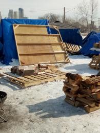 Several of the structures and the fire pit at the encampment in Near North, with snow on the ground and some of the Minneapolis skyline in back.