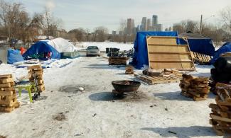 Several of the tents and the fire pit at the encampment in Near North, with snow on the ground and the Minneapolis skyline in back.
